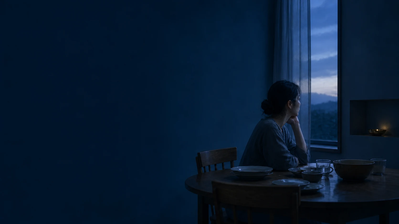 夜の食卓で、窓の外を見ている女性。